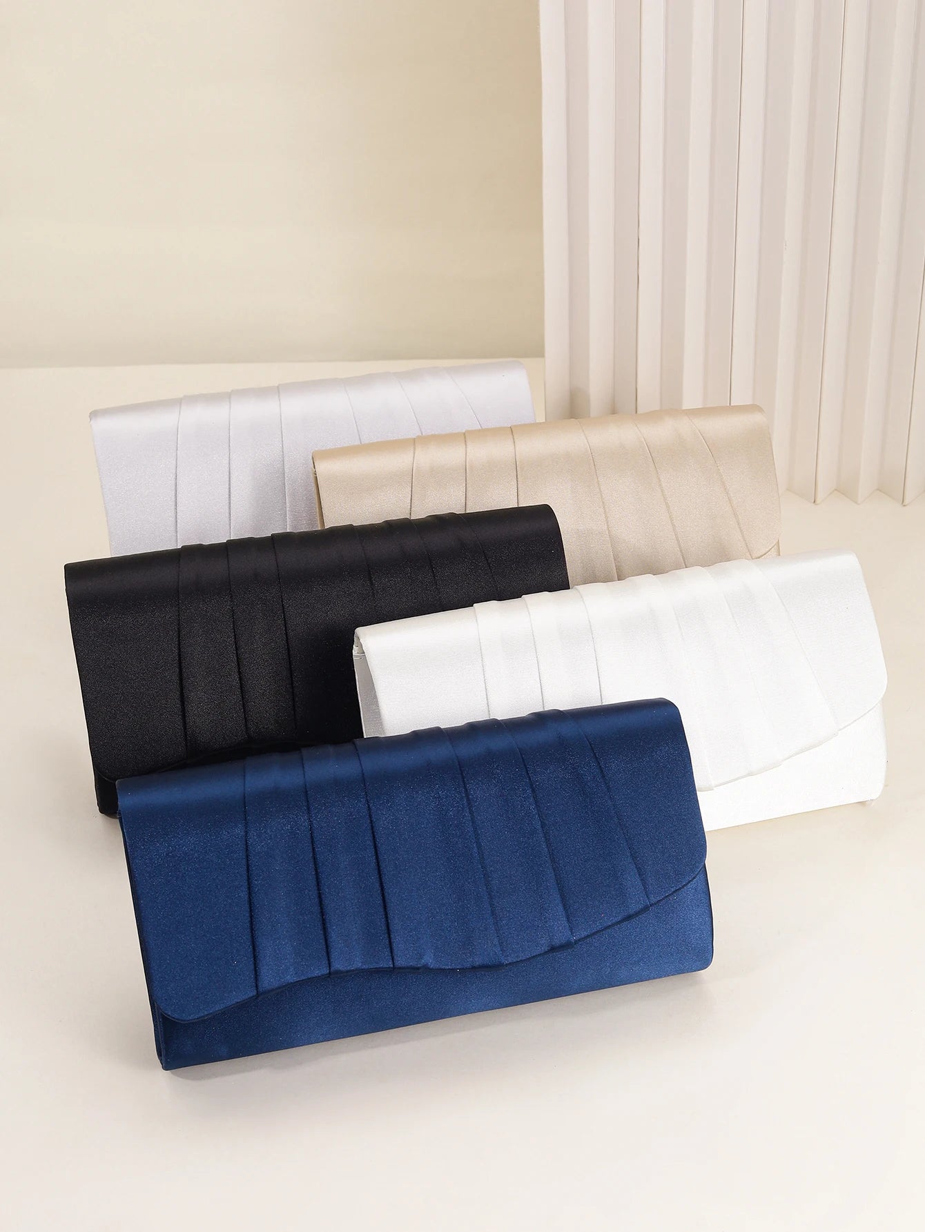 Pleated envelope style clutch held by model showing slim elegant design, women’s evening handbag for formal occasions