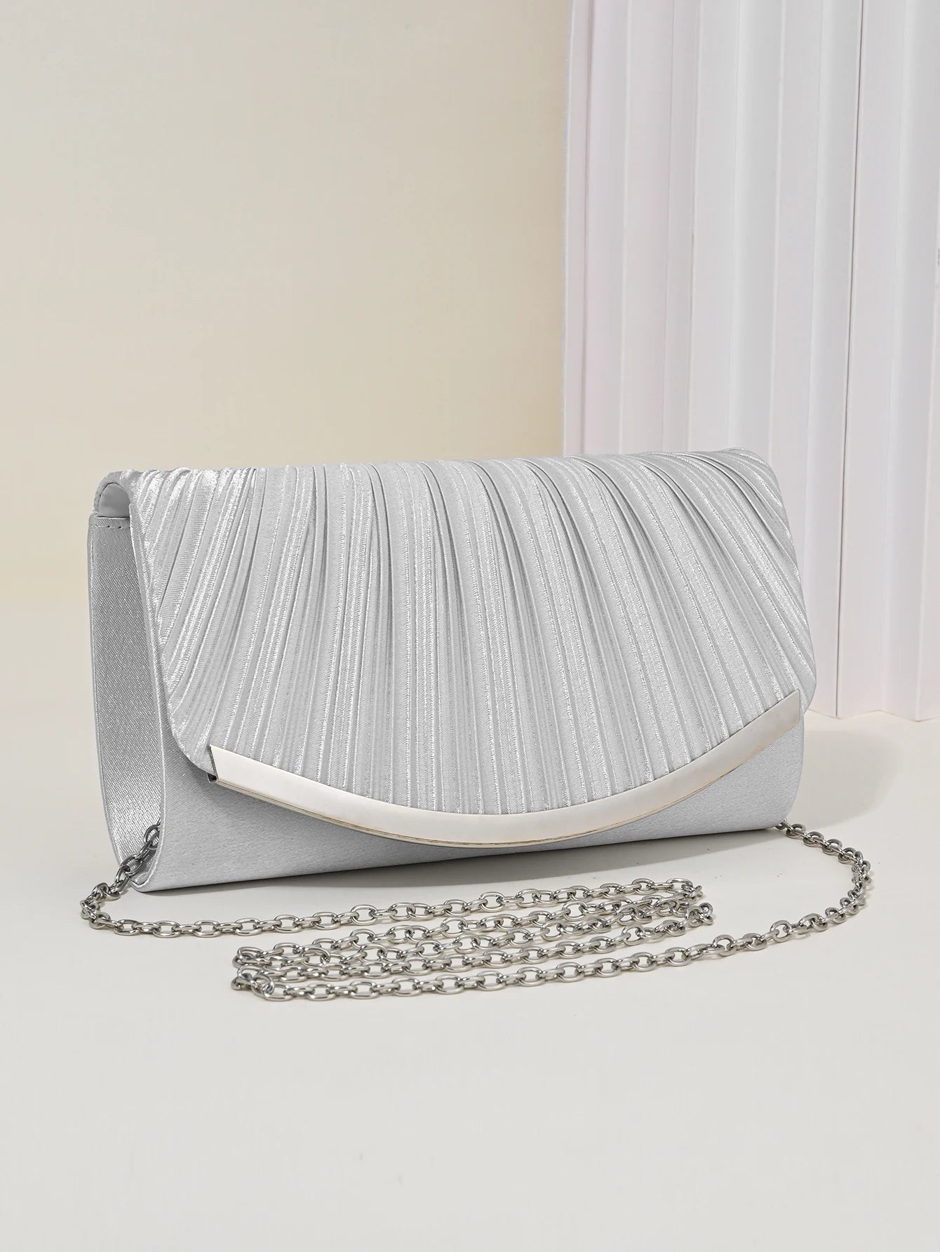 Pleated metallic clutch held by model showing slim structured silhouette, women’s elegant evening handbag with detachable chain strap